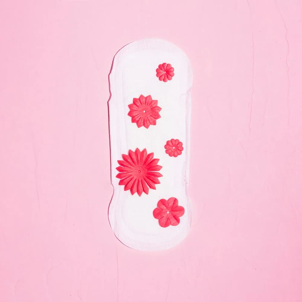 A white sanitary pad on a pink background, scattered with small red paper flowers