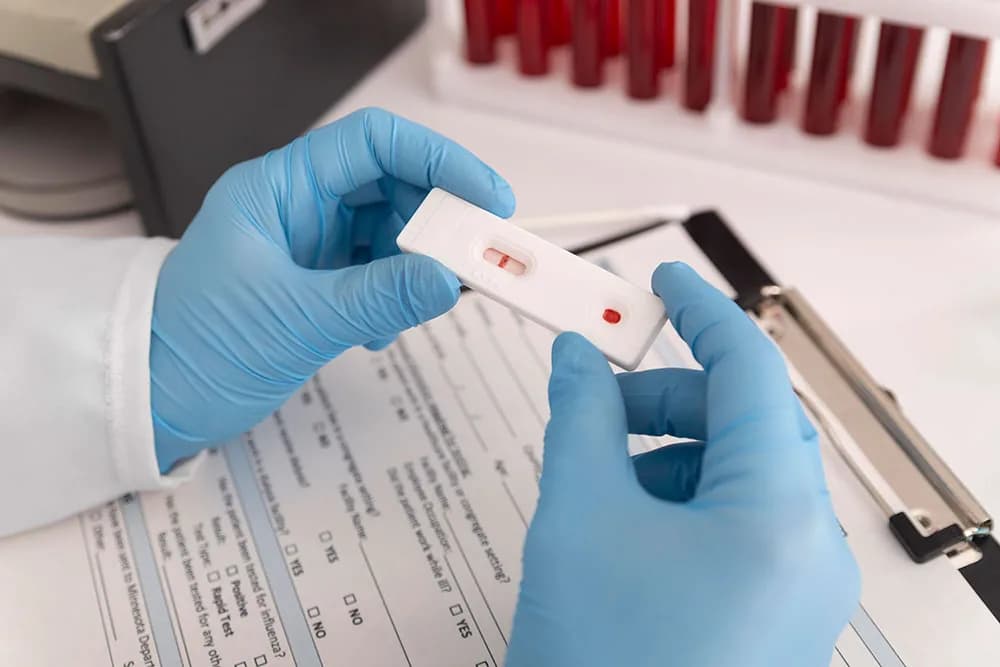 Gloved hands holding a rapid test cassette over a laboratory request form, with a rack of blood collection tubes behind